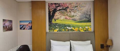 Una habitación de hotel con una cama, una mesita de noche de madera, una lámpara y dos cuadros en la pared.