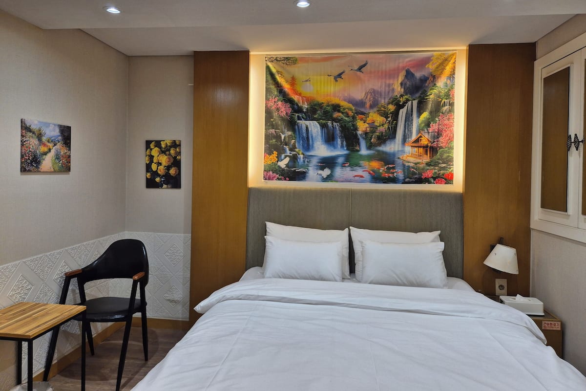 A hotel room with a bed, a desk, a chair, and a painting of a waterfall.