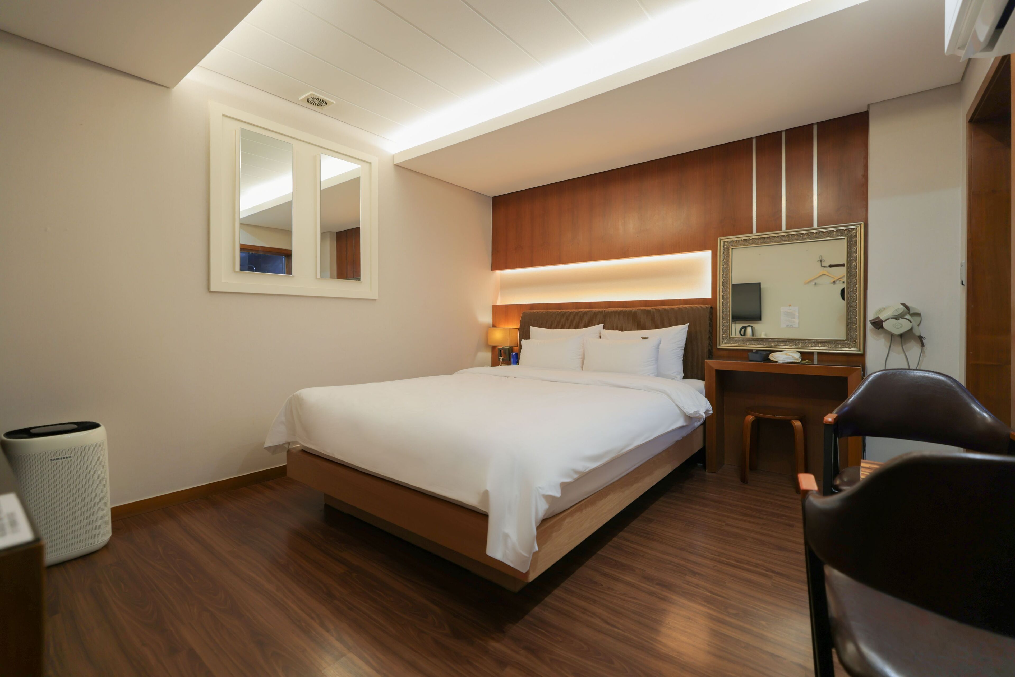 A hotel room with a bed, a bedside table, a mirror, a chair, and a trash bin.