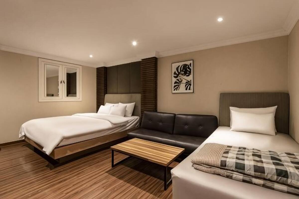 A hotel room with a bed, a sofa, a small table, a mirror, and a wall-mounted artwork.