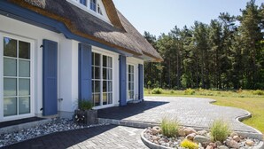 Una casa con tejado de paja, contraventanas azules y un camino empedrado que conduce a un jardín ajardinado con un borde de piedra circular.