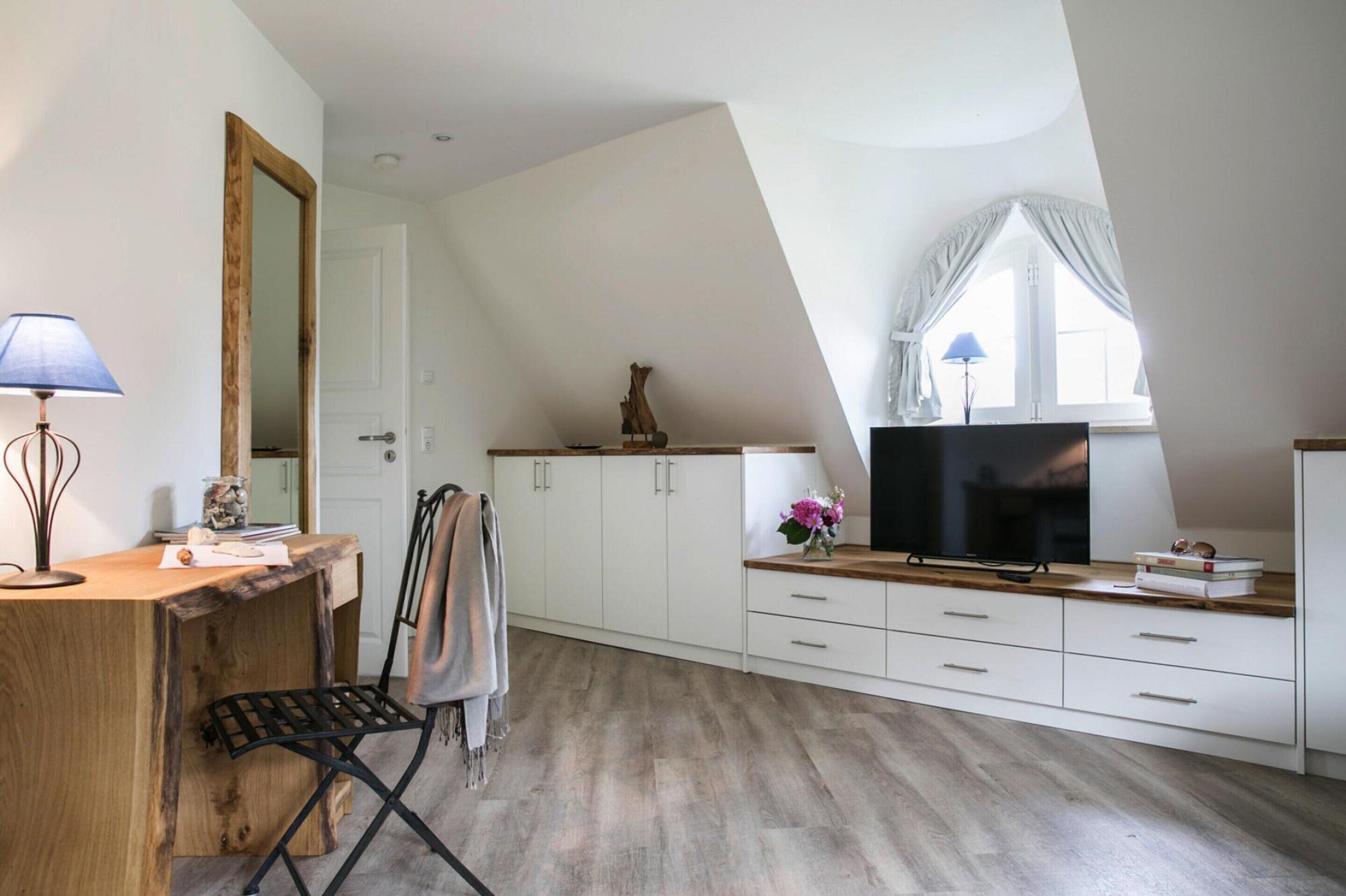Une cuisine moderne avec un comptoir en bois, des armoires blanches, une chaise noire et une grande fenêtre avec des rideaux.