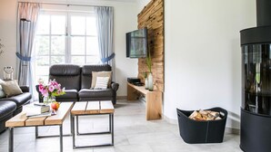 Una sala de estar moderna con un sofá de cuero negro, una mesa de centro de madera, un televisor montado en una pared de madera y una chimenea negra.