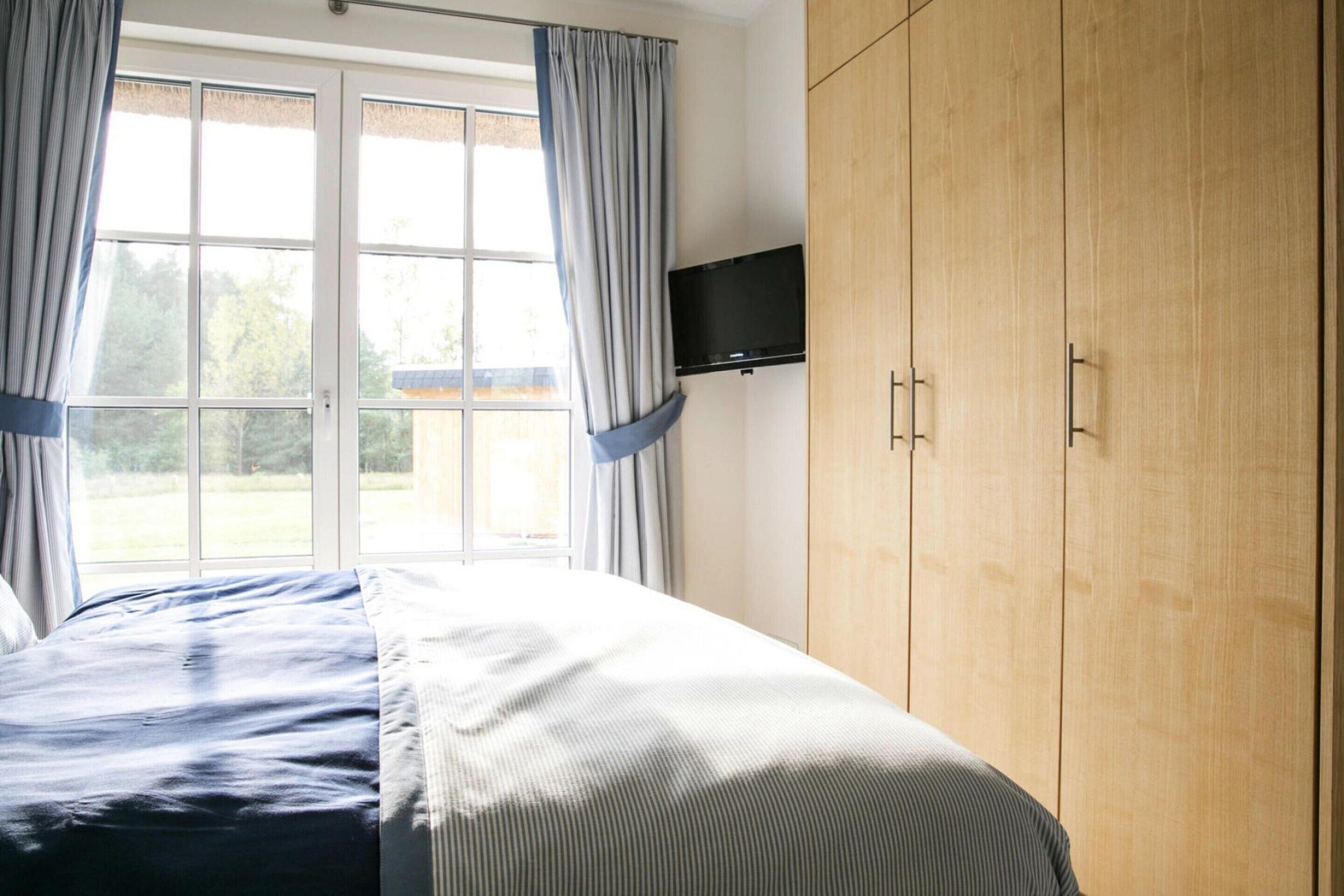 Ein Schlafzimmer mit Bett, Kleiderschrank, Fernseher und einem Fenster mit Vorhängen.