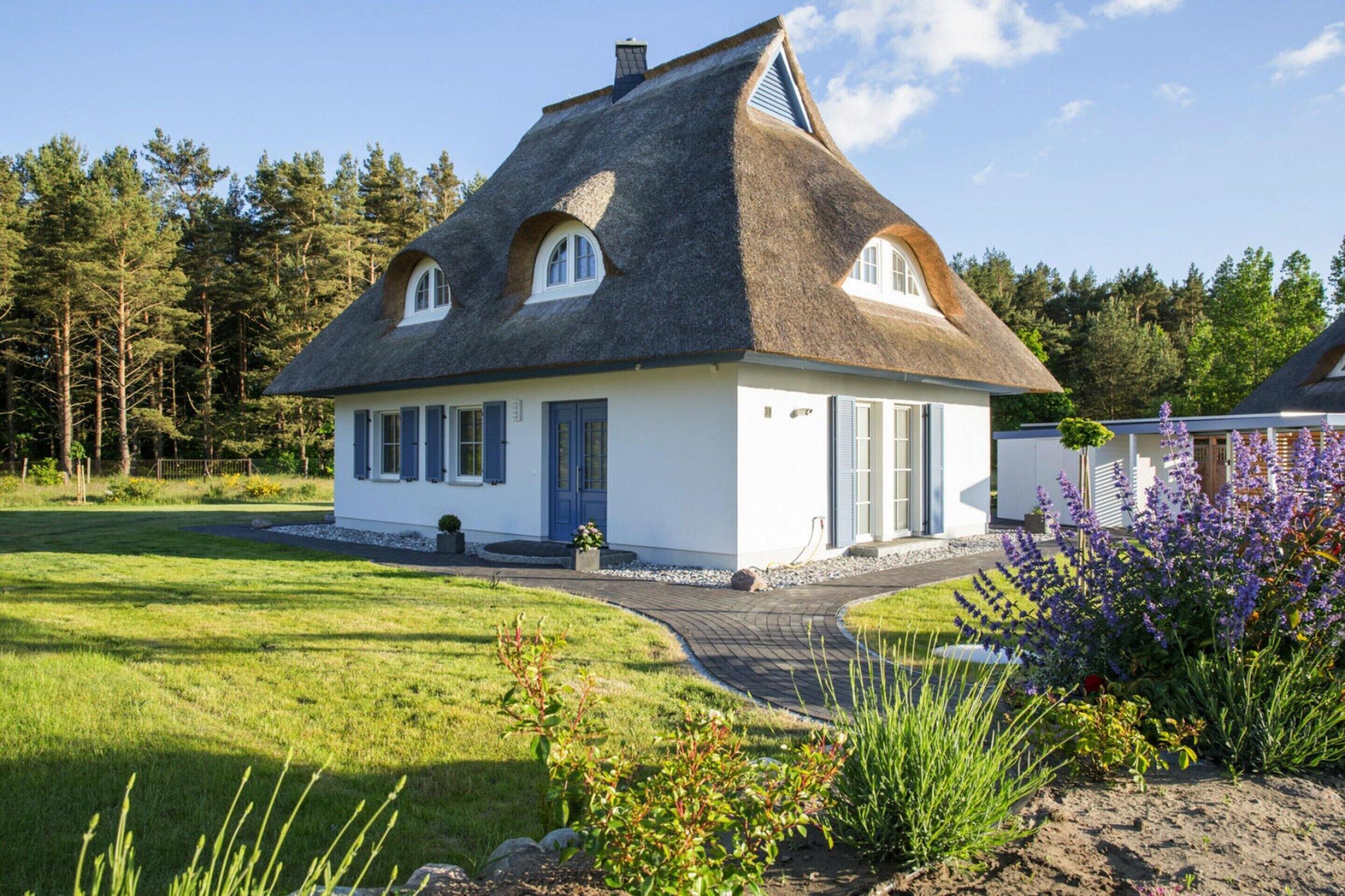 Ein weißes Haus mit Strohdach, einer Veranda und einem gepflegten Garten mit verschiedenen Pflanzen.