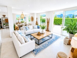 Un salon moderne avec un canapé, une table basse et de grandes fenêtres donnant sur un paysage verdoyant et des montagnes.