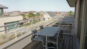Ein Balkon mit Tisch und Stühlen, der auf einen Wohnbereich mit Häusern und einem klaren Himmel blickt.