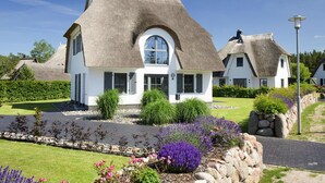 Una casa con techo de paja, paredes blancas y un jardín bien cuidado con diversas plantas y flores.