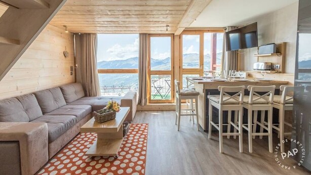 A modern interior with a sofa, dining table, chairs, a kitchen area, and large windows offering a mountain view.