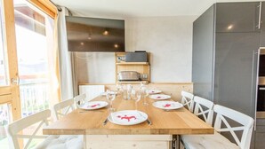 A dining area with a wooden table set for six, white chairs, and a television above the table.