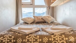 A neatly made bed with patterned bedding and pillows, a window with a mountain view, and a lamp on the bedside table.