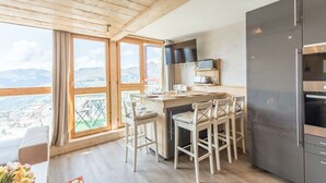 A modern kitchen with a large island, wooden ceiling, and a view of mountains.