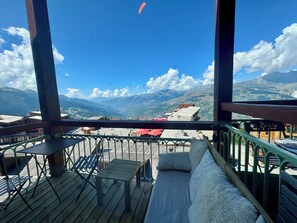A balcony with a view of mountains, a wooden table, and a cushioned bench.