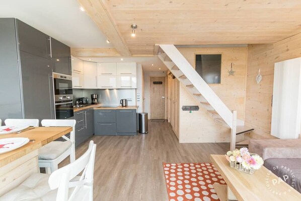 A modern kitchen with grey cabinets, a wooden dining table, and a staircase leading to another level.