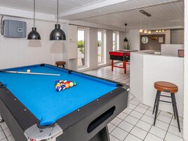 Una mesa de billar con bolas, una mesa de fútbol de mesa y una zona de bar con taburetes.