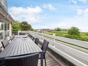 A deck with a table and chairs, overlooking a grassy area and a body of water. - 4 Star Holiday Home in Thyholm (Thyholm)