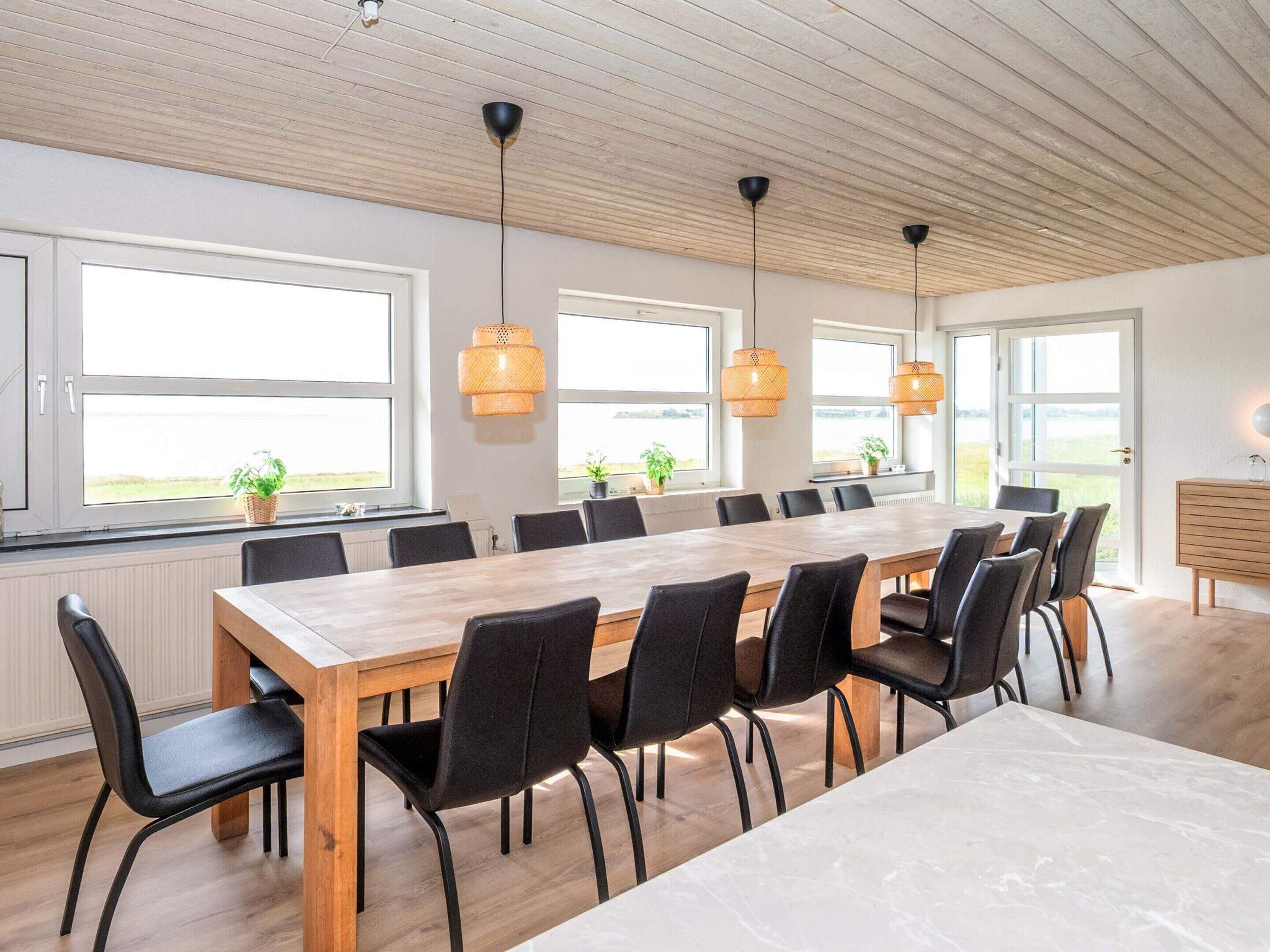 A spacious dining area with a long wooden table, black chairs, and hanging wicker lamps.