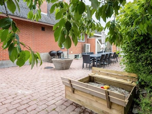 An outdoor patio with a brick floor, a concrete planter, a wooden bench, and a brick wall in the background. - 4 Star Holiday Home in Thyholm (Thyholm)