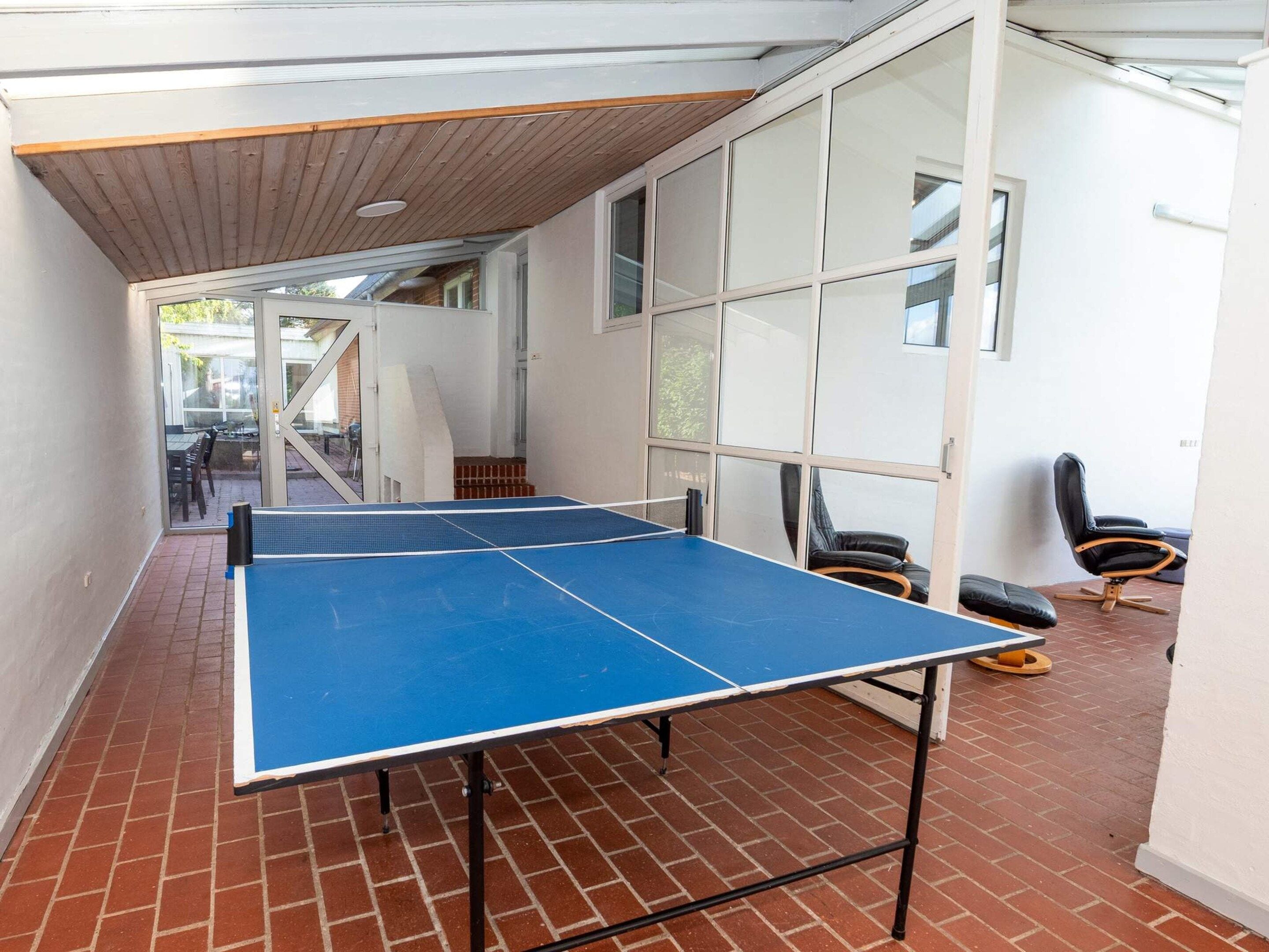 Une table de ping-pong dans une pièce dont le sol est en briques, les murs sont blancs et le plafond est en bois.