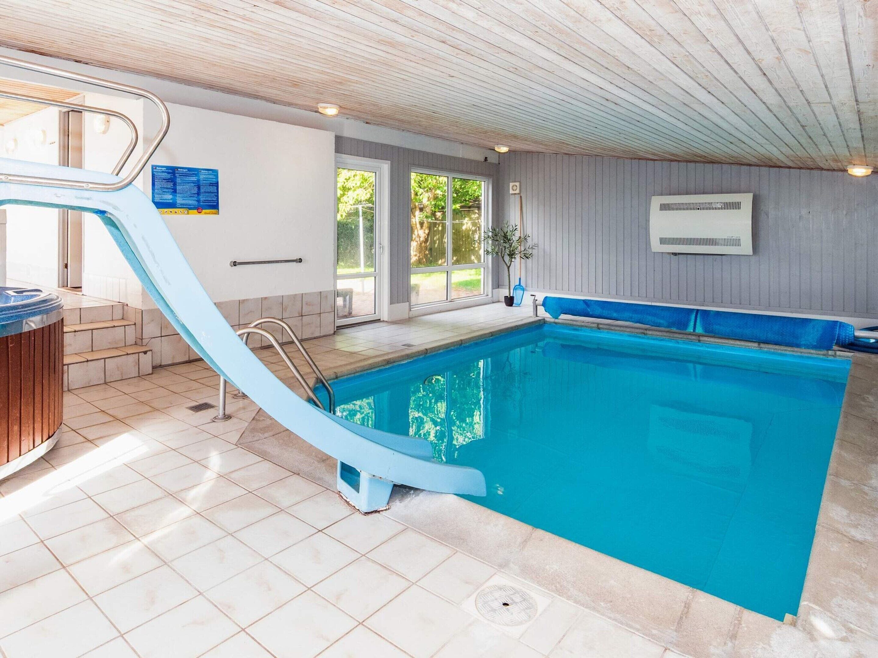 A swimming pool with a blue slide, a hot tub, and a view of the outdoors.
