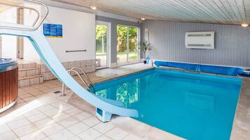 A swimming pool with a blue slide, a hot tub, and a view of the outdoors.