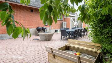 An outdoor patio with a brick floor, a concrete planter, a wooden raised bed, and a brick building in the background.