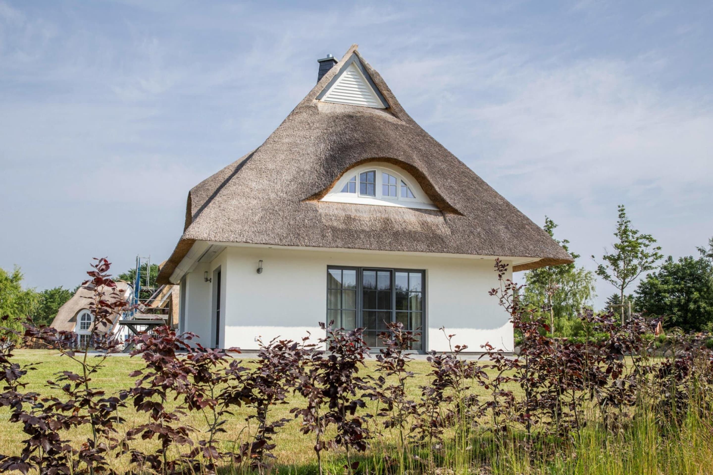 Une maison avec un toit de chaume, une façade blanche et une grande fenêtre.