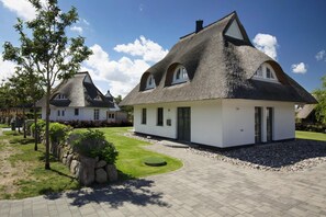 A modern house with a thatched roof, a paved driveway, and a well-maintained garden.