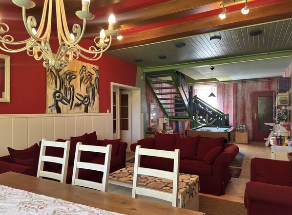 Un salon chaleureux avec des canapés rouges, une table basse en bois et un lustre. Un escalier mène à une mezzanine offrant une vue sur la ville.