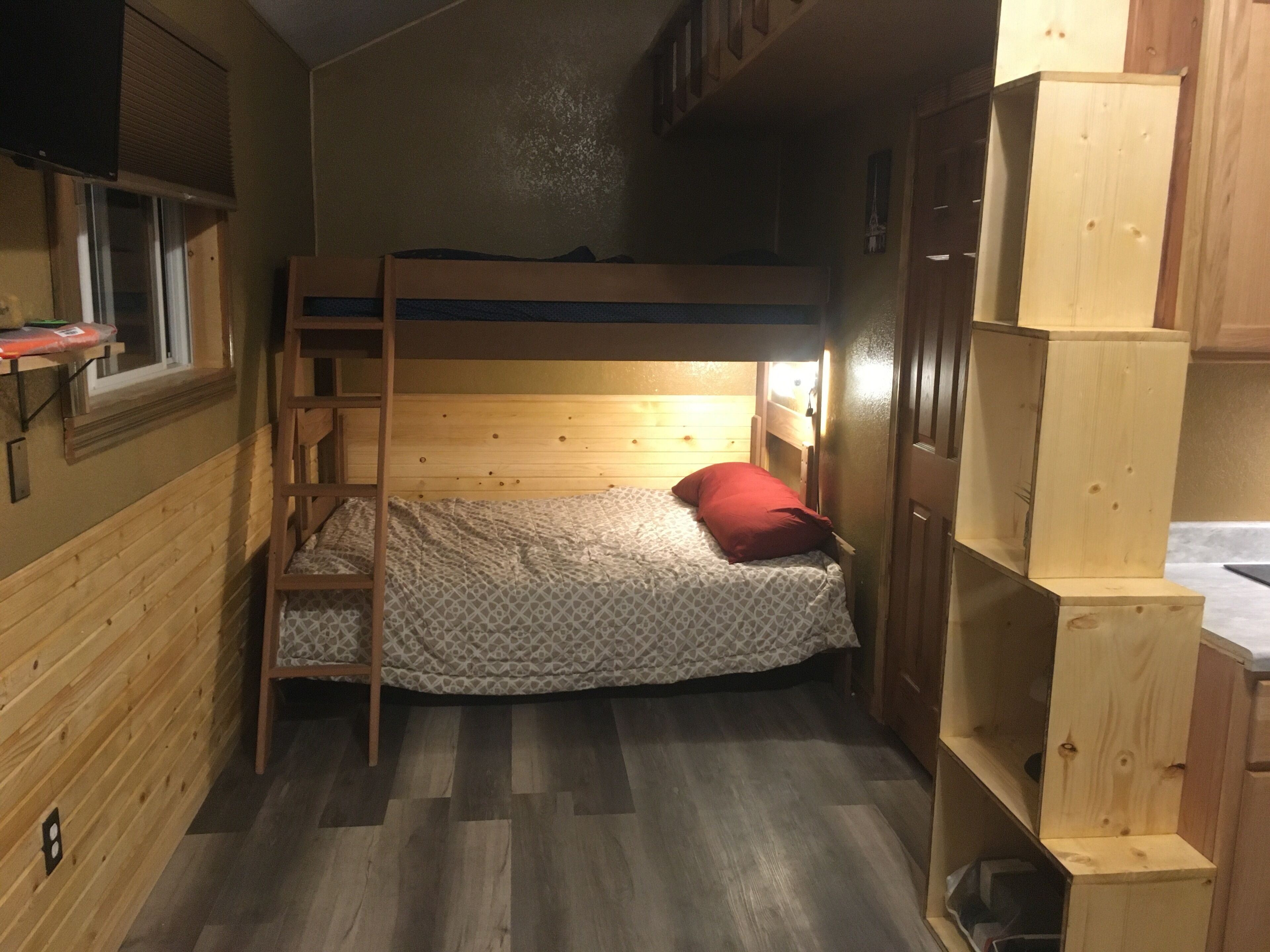 A small, compact room with a bunk bed, a wooden desk, and a small window.
