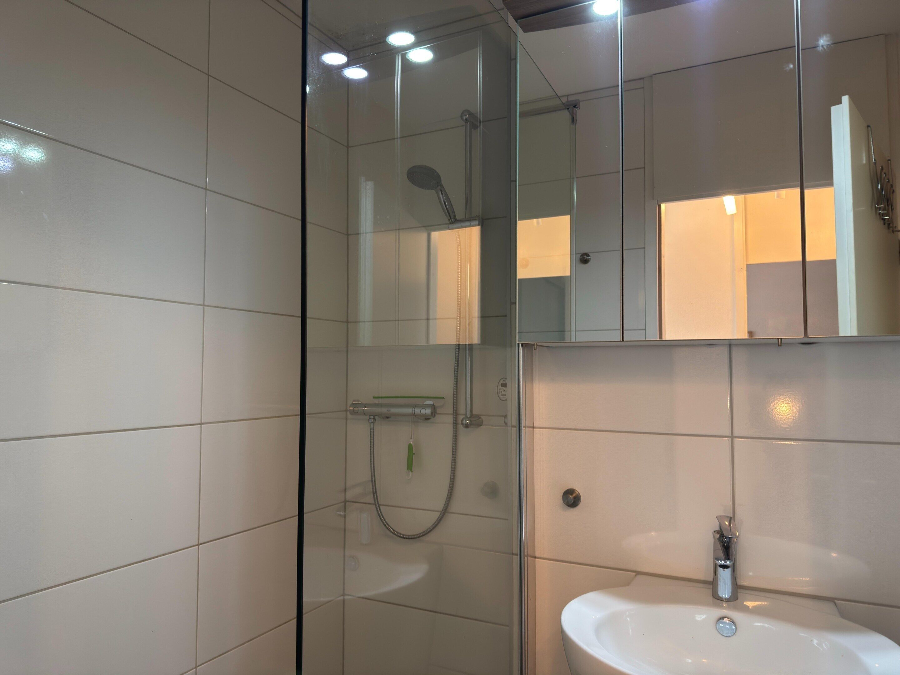 A modern bathroom with a glass-enclosed shower, a sink, and a mirror.