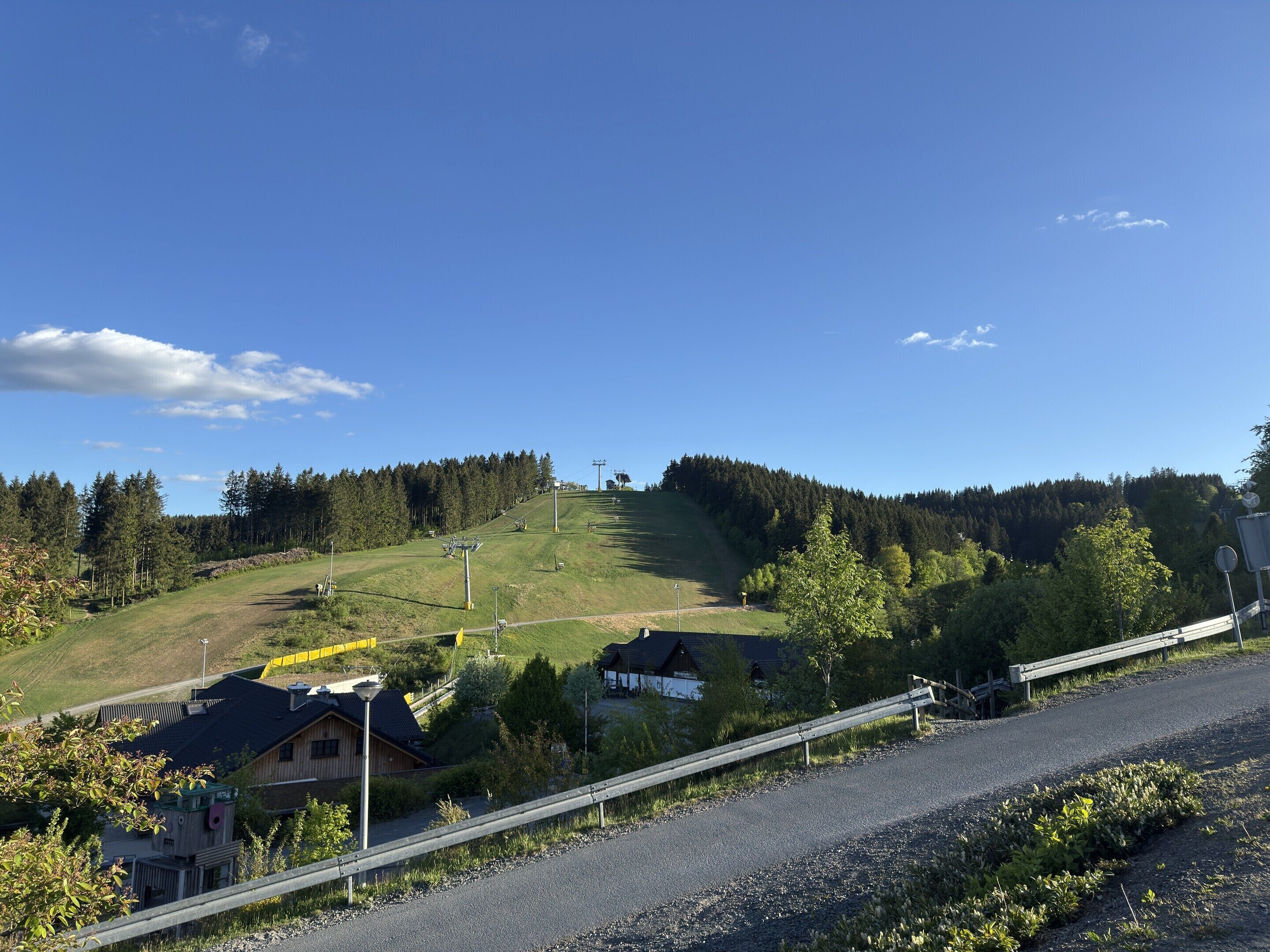 A rural landscape with a ski lift, houses, and a forested hill.