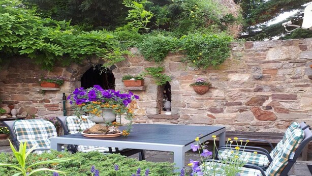 An outdoor patio with a stone wall, a table, and chairs. - Ferienwohnung Nahe Wernigerode (Wernigerode)