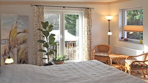 A bedroom with a bed, a potted plant, a chair, a table, and a window with curtains. - Ferienwohnung Nahe Wernigerode (Wernigerode)