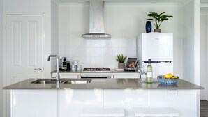 A modern kitchen with white cabinetry, stainless steel appliances, a central island with a sink, and a built-in oven. - Whale of a Time - Vasse: Your Perfect Retreat for Comfort and Nature (Vasse)