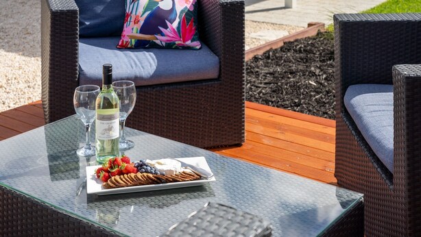 A glass table with a bottle of wine, glasses, and a plate of food. - Whale of a Time - Vasse: Your Perfect Retreat for Comfort and Nature (Vasse)