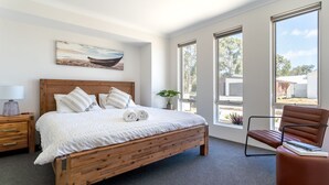 A bedroom with a wooden bed, white bedding, a painting on the wall, and large windows. - Whale of a Time - Vasse: Your Perfect Retreat for Comfort and Nature (Vasse)