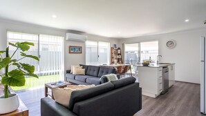 A modern apartment with a grey sofa, a dining area, a kitchen, and a balcony with large windows. - Whale of a Time - Vasse: Your Perfect Retreat for Comfort and Nature (Vasse)