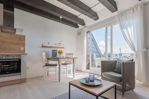 Une cuisine moderne dotée d’un four encastré, un coin repas avec une table et des chaises, et une grande porte-fenêtre coulissante donnant sur un balcon extérieur.