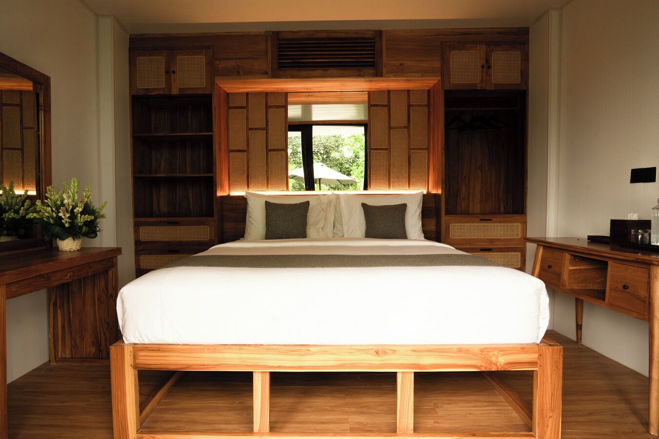 A bedroom with a large bed, wooden headboard, built-in bookshelves, and a window with a view of greenery.