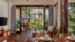 Uma sala de jantar com mesa posta para quatro pessoas, um sofá de vime e vista para a piscina e o jardim.