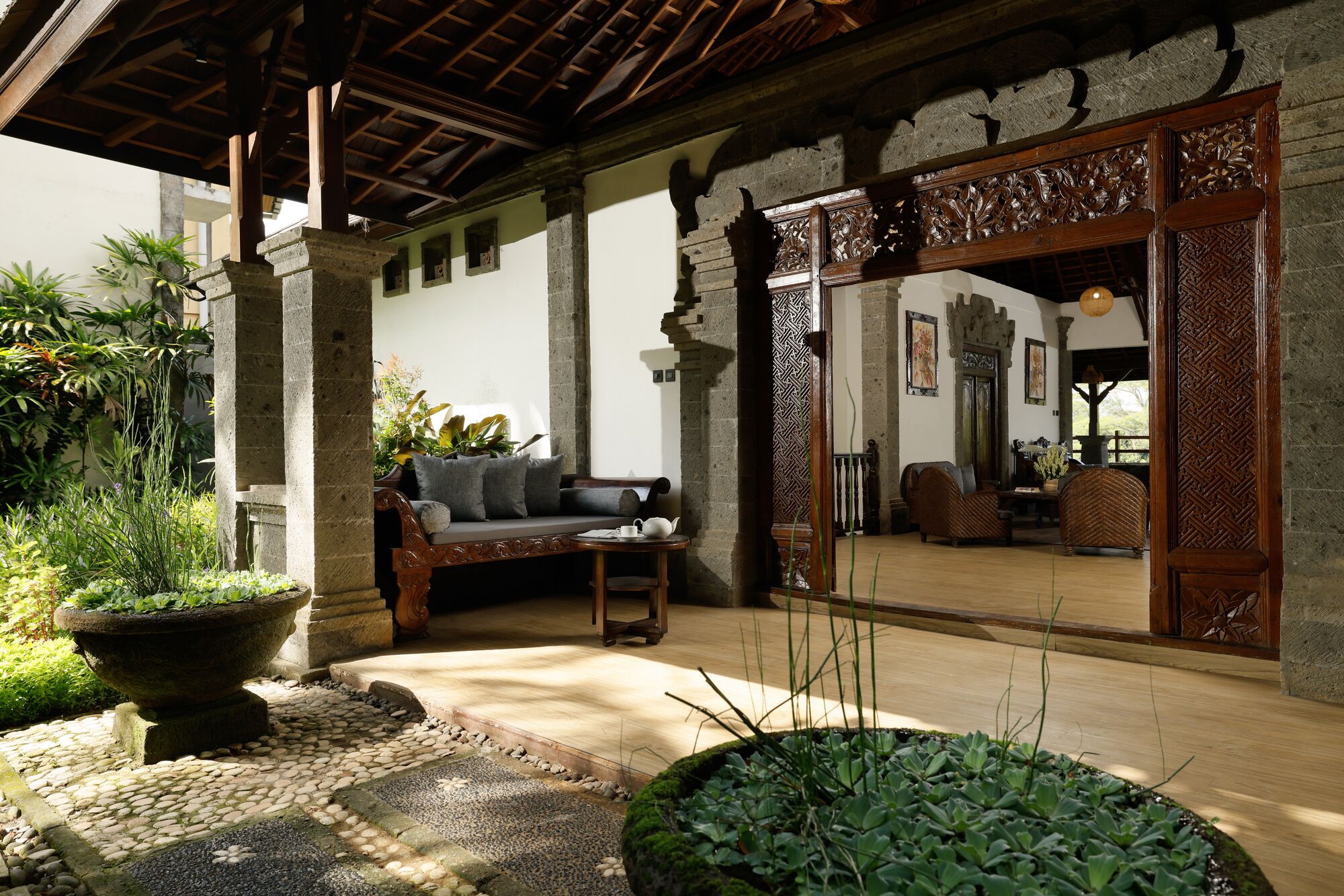A traditional wooden structure with a stone pillar, a sofa, and a table with a teapot.