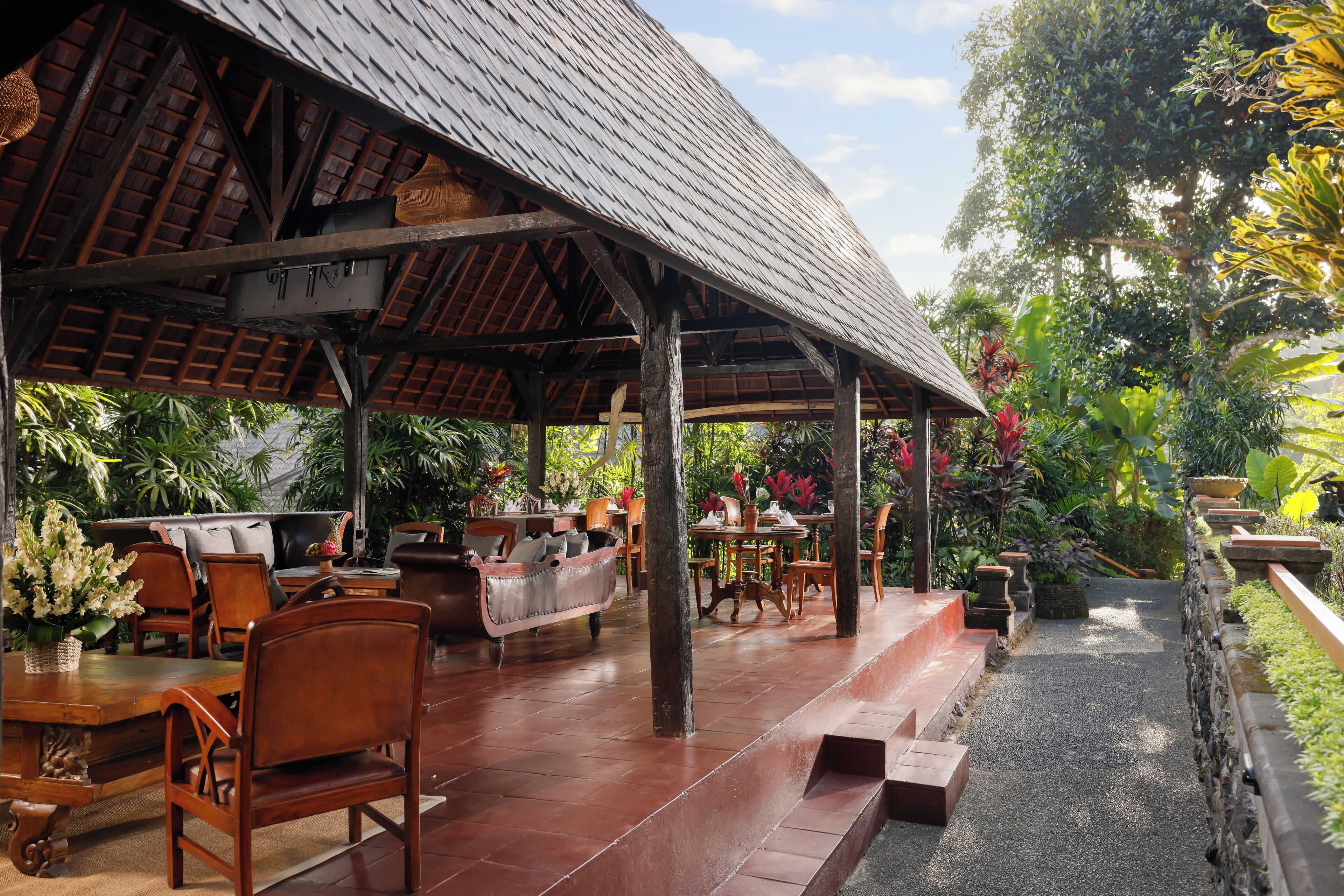 A covered outdoor seating area with wooden furniture and a thatched roof.