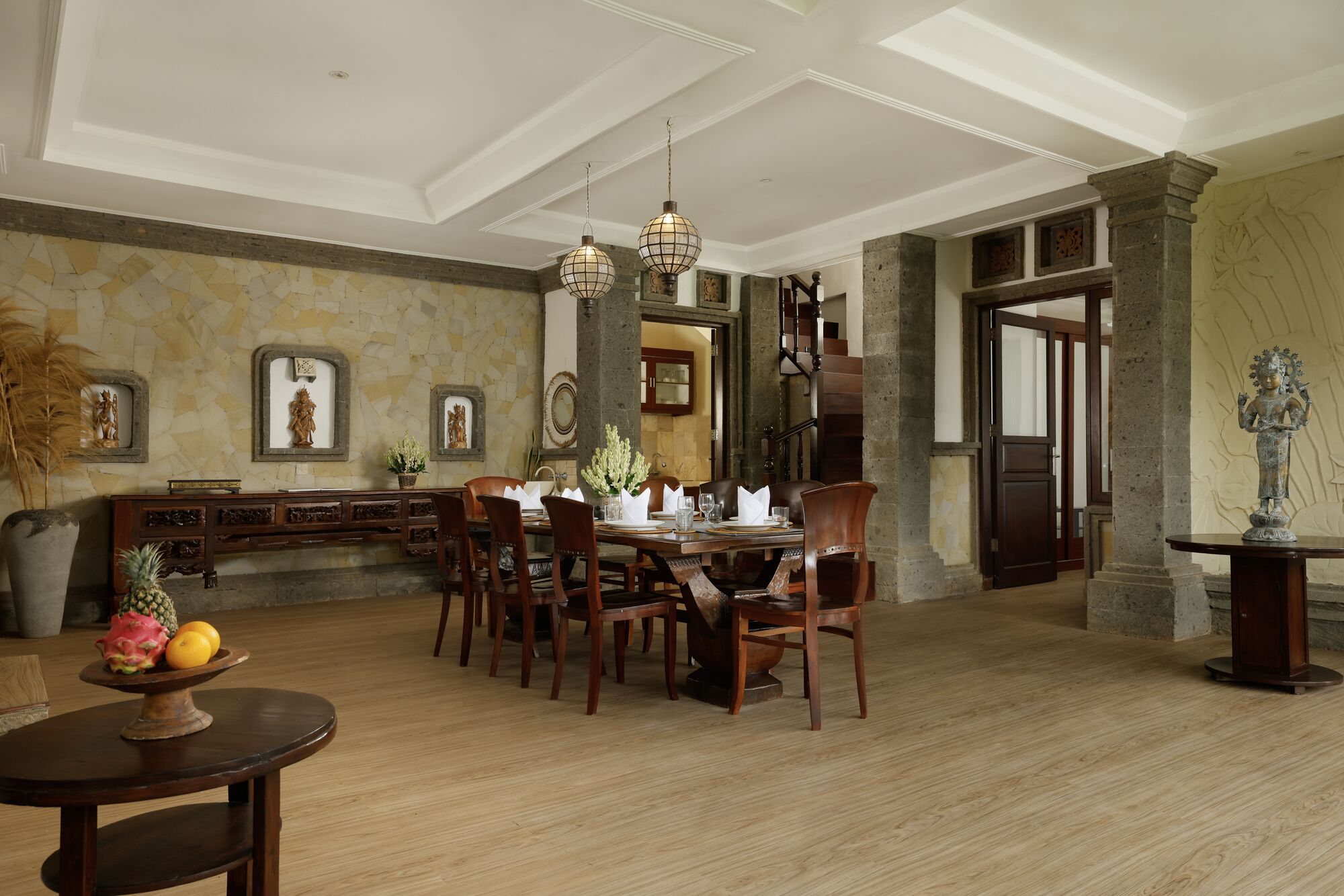 A dining area with a wooden table and chairs, a stone wall with framed artwork, and a staircase leading to another level.