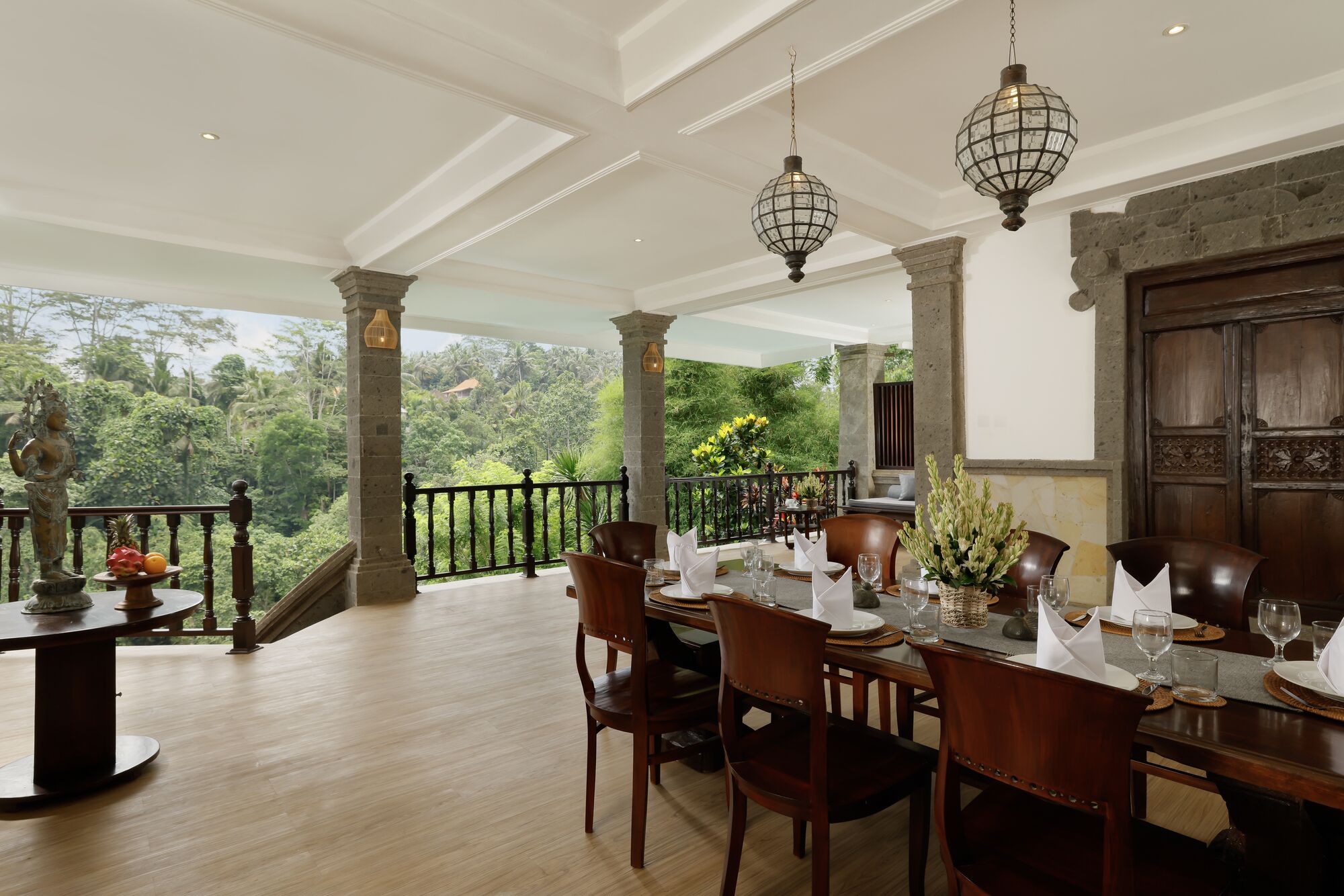 A dining area with a view of lush greenery, wooden furniture, and a stone wall.