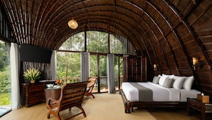 Um quarto espaçoso com uma cama grande, móveis de madeira e vista para a floresta através de janelas amplas.
