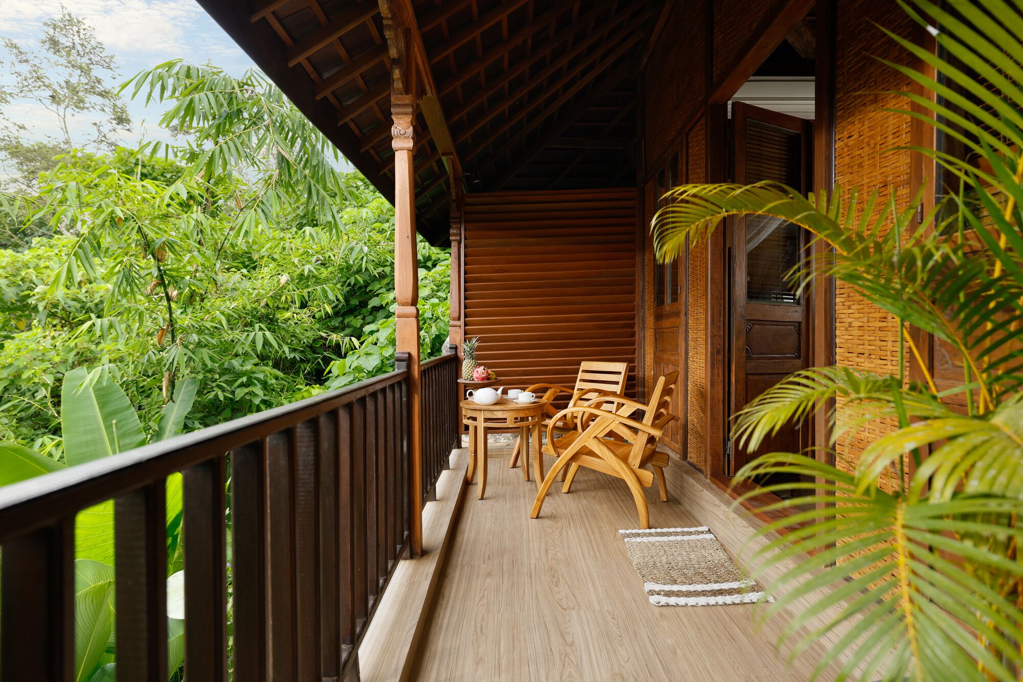 A wooden balcony with a table and chairs, surrounded by lush greenery.