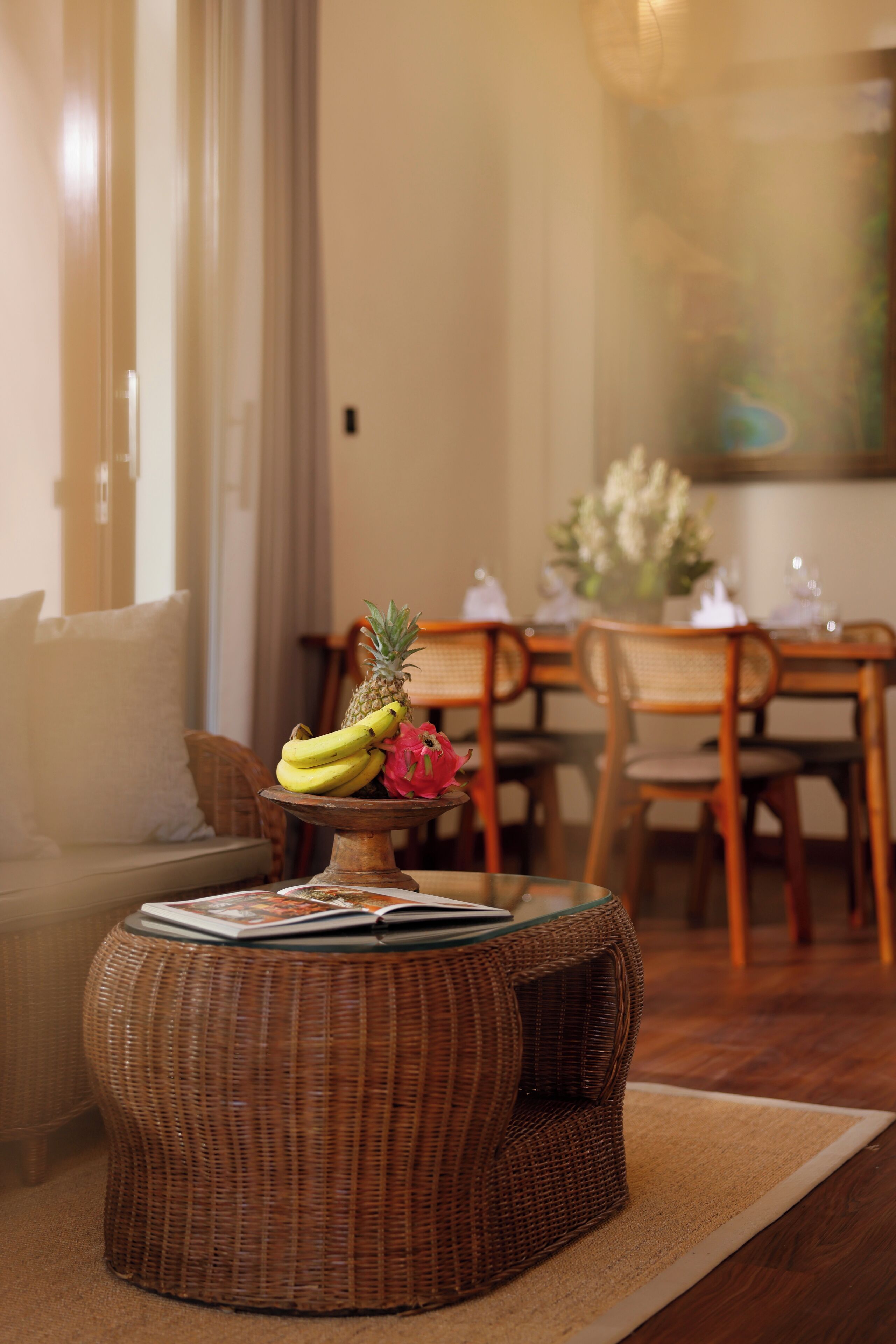 A dining area with wicker furniture, a table with a fruit centerpiece, and a sofa with a cushion.