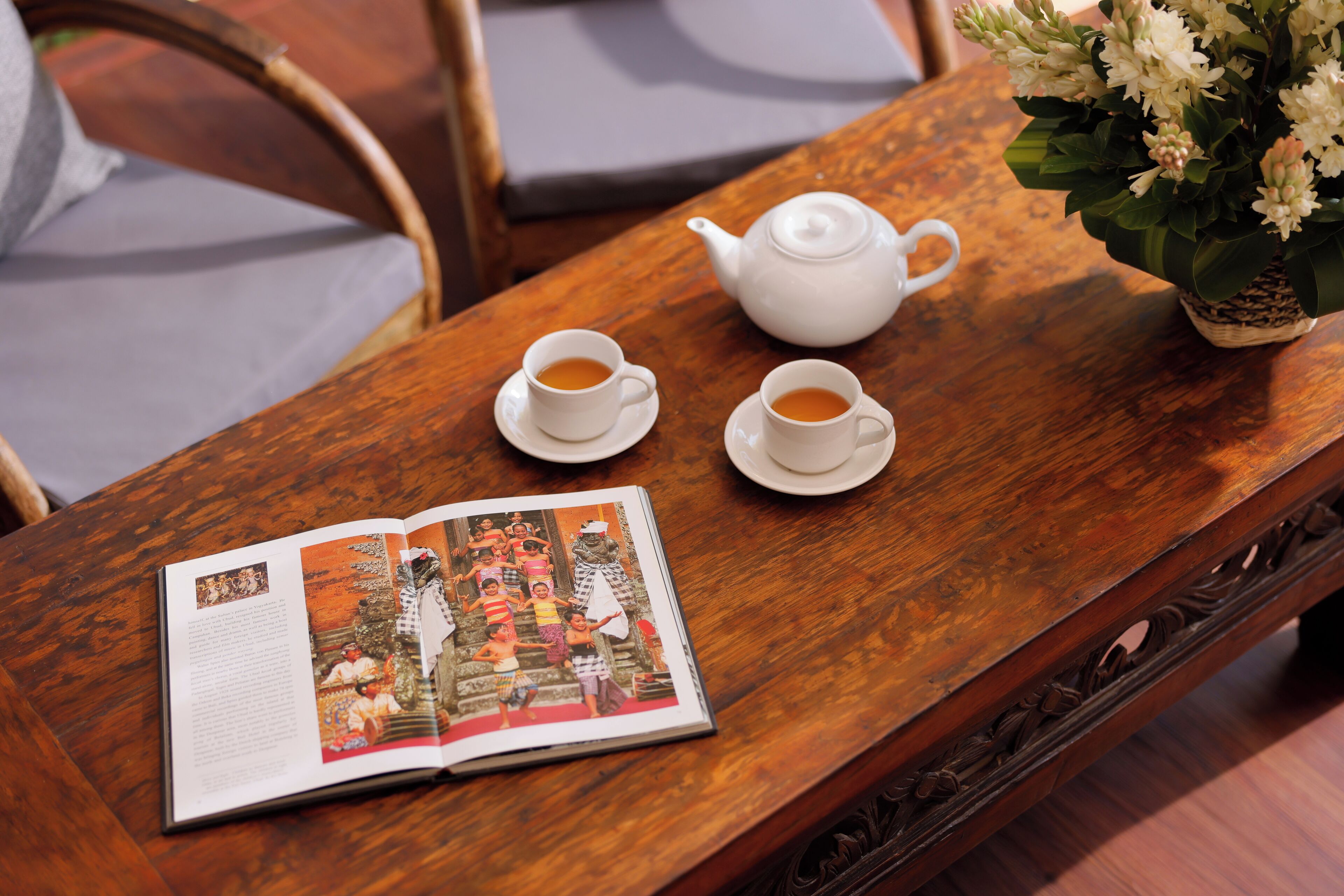 A wooden table with a white teapot, two cups of tea, and an open magazine.