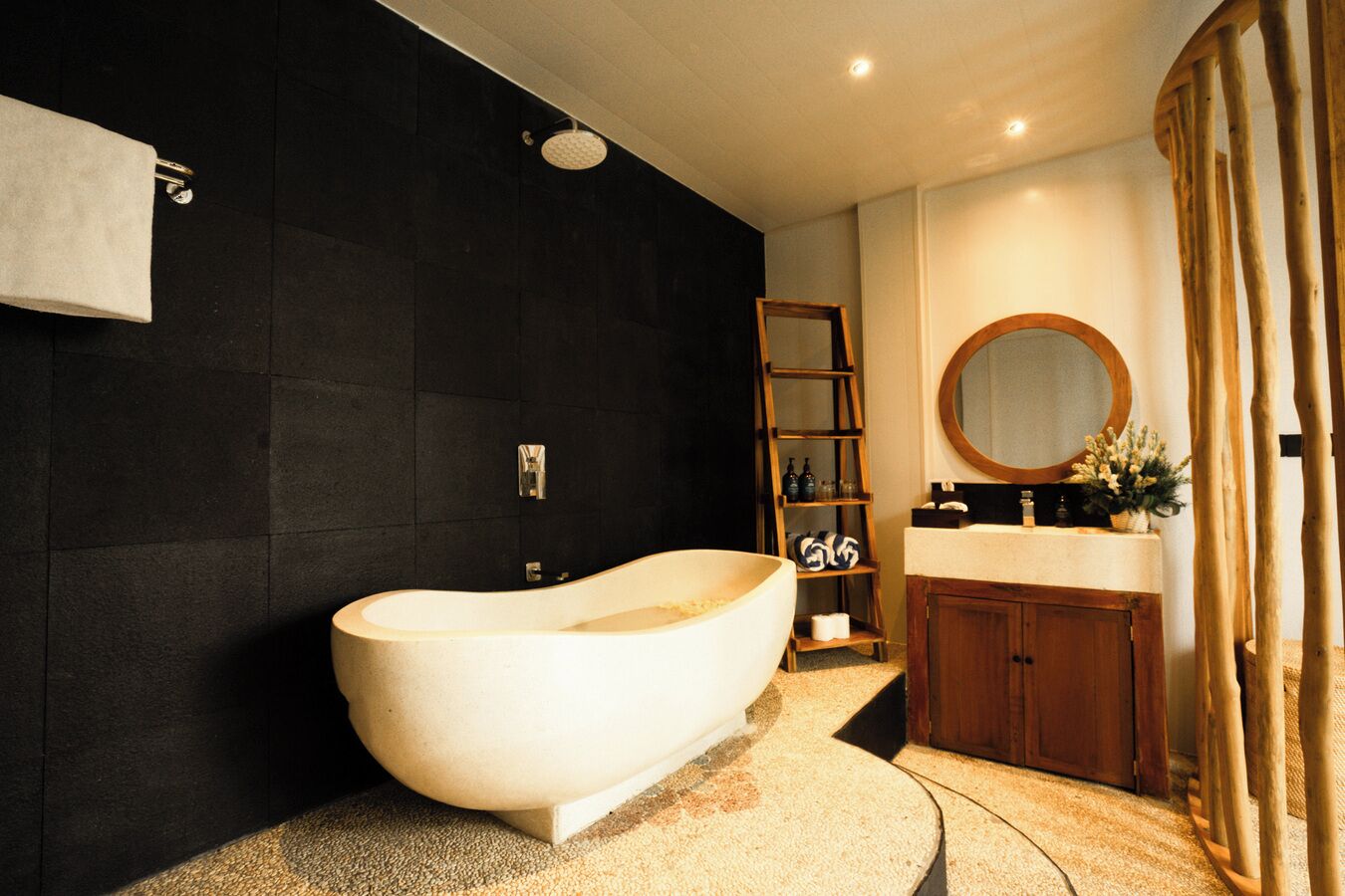 A modern bathroom with a freestanding bathtub, a wooden ladder shelf, a round mirror, and a wooden cabinet.